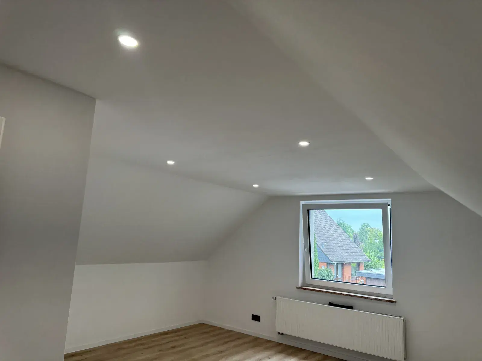 Fertiges Zimmer im Dachgeschoss mit Dachschrägen, Einbauspots, Fenster mit Heizkörper und hellem Boden